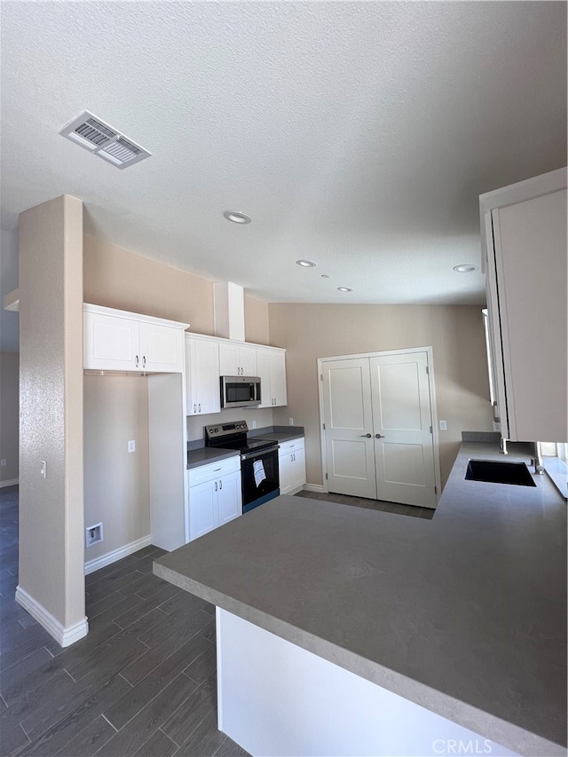 kitchen with kitchen peninsula, a textured ceiling, white cabinetry, dark hardwood / wood-style floors, and stainless steel appliances