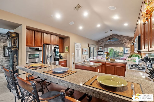 kitchen with kitchen peninsula, ceiling fan, a breakfast bar area, lofted ceiling, and stainless steel appliances