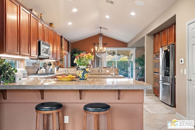 kitchen featuring kitchen peninsula, a breakfast bar area, vaulted ceiling, and appliances with stainless steel finishes