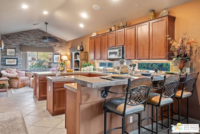 kitchen with a kitchen breakfast bar, kitchen peninsula, light tile patterned floors, a kitchen island with sink, and lofted ceiling