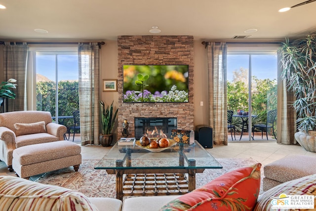 living room with light tile patterned flooring, plenty of natural light, and a stone fireplace