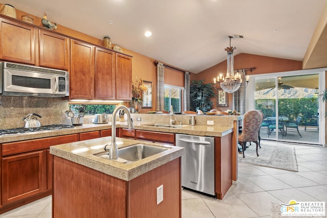 kitchen featuring pendant lighting, stainless steel appliances, sink, vaulted ceiling, and a center island with sink