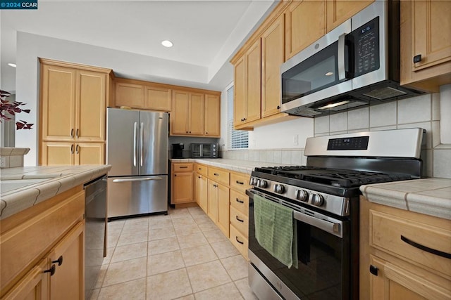 kitchen featuring light brown cabinets, tile countertops, backsplash, light tile patterned floors, and appliances with stainless steel finishes