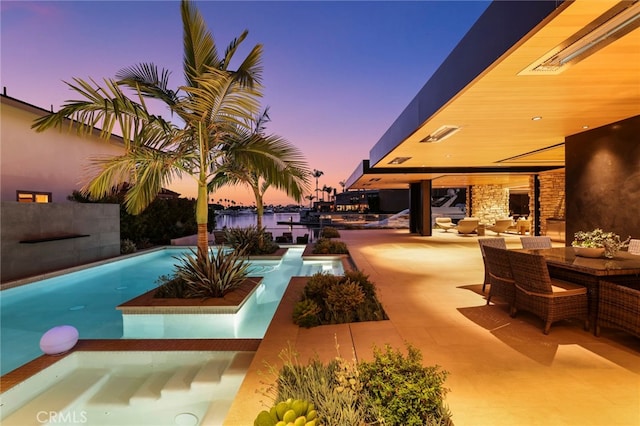 pool at dusk featuring a patio area, an in ground hot tub, an outdoor hangout area, and a water view