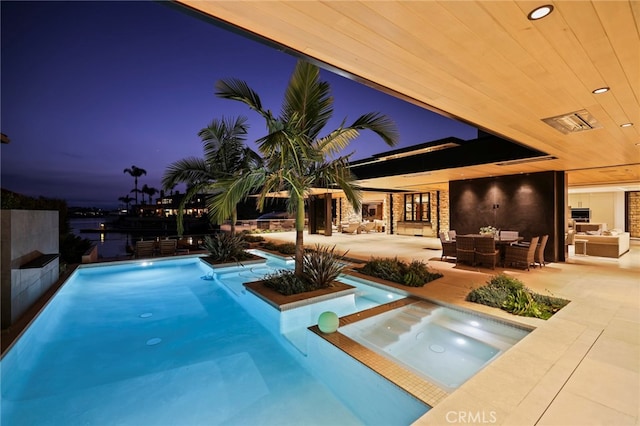 pool at dusk featuring an in ground hot tub, a patio area, and an outdoor living space