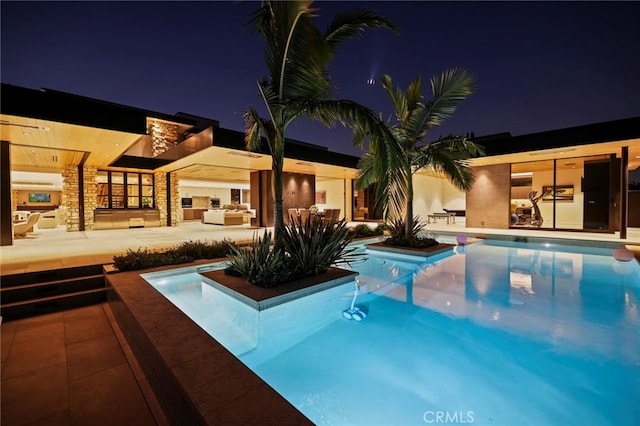 pool at night with a patio and area for grilling