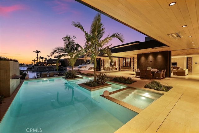 pool at dusk featuring a patio, an in ground hot tub, and an outdoor hangout area