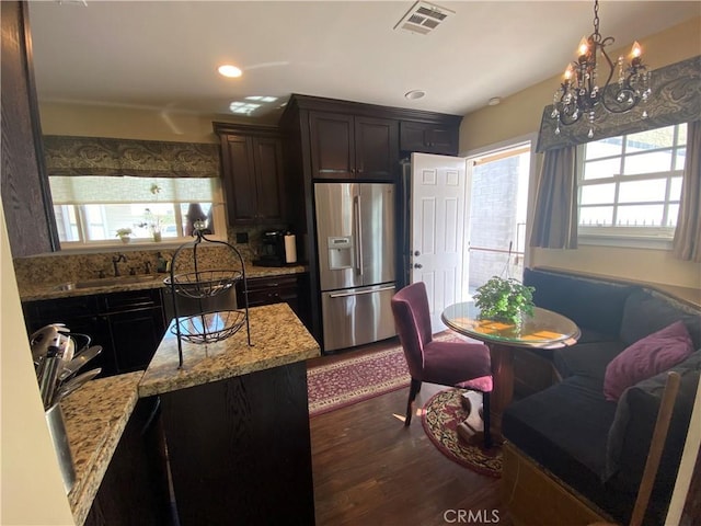 kitchen with light stone countertops, stainless steel refrigerator with ice dispenser, dark hardwood / wood-style flooring, sink, and dark brown cabinets