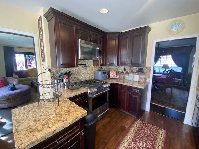 kitchen featuring light stone countertops, dark wood-type flooring, backsplash, and appliances with stainless steel finishes