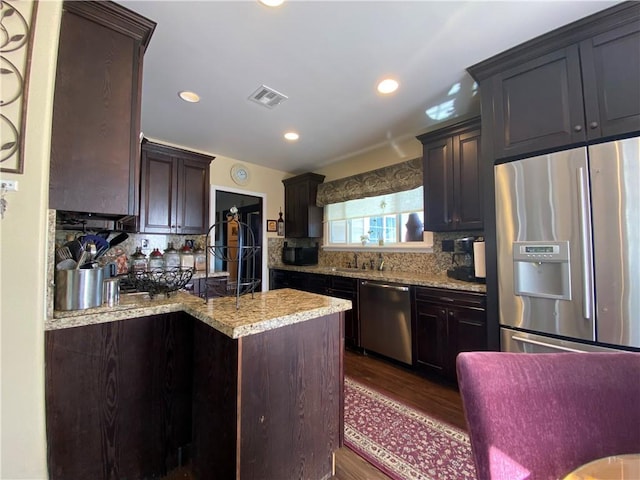 kitchen featuring appliances with stainless steel finishes, dark wood-type flooring, backsplash, light stone counters, and dark brown cabinets