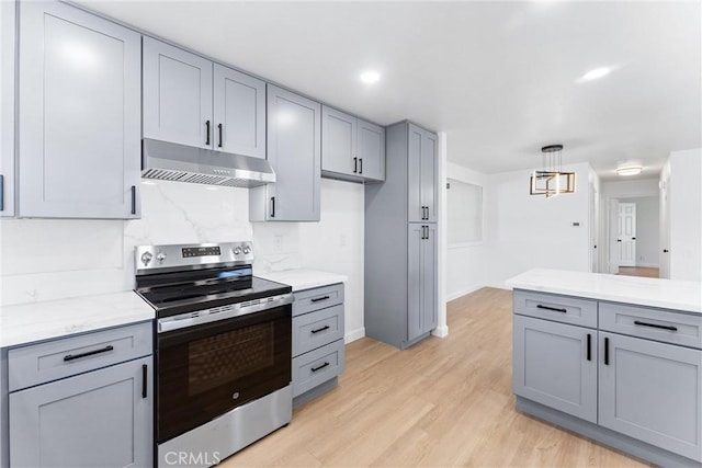 kitchen featuring gray cabinetry, light wood-type flooring, stainless steel electric range oven, tasteful backsplash, and decorative light fixtures