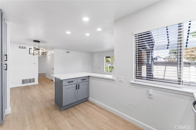 kitchen featuring kitchen peninsula, gray cabinets, light hardwood / wood-style flooring, and pendant lighting