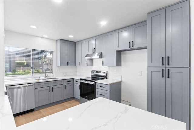 kitchen featuring light stone countertops, sink, appliances with stainless steel finishes, and light hardwood / wood-style flooring