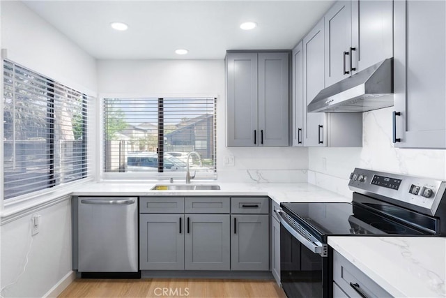 kitchen with appliances with stainless steel finishes, light wood-type flooring, light stone counters, gray cabinetry, and sink