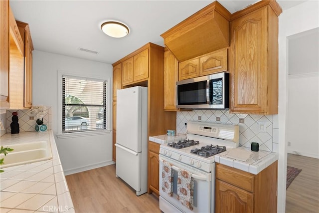 kitchen with sink, tile countertops, white appliances, decorative backsplash, and light wood-type flooring