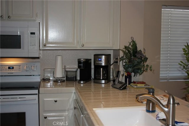 kitchen with stove, white microwave, sink, tile counters, and white cabinetry