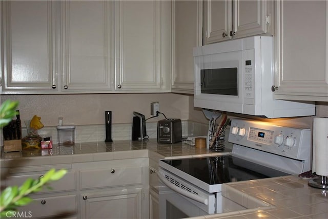 kitchen with tile countertops, white cabinets, and white appliances