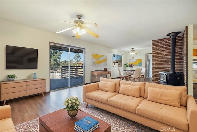 living room with ceiling fan, a wood stove, and dark wood-type flooring