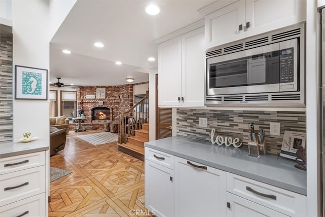 kitchen featuring stainless steel microwave, backsplash, light parquet floors, white cabinets, and a fireplace