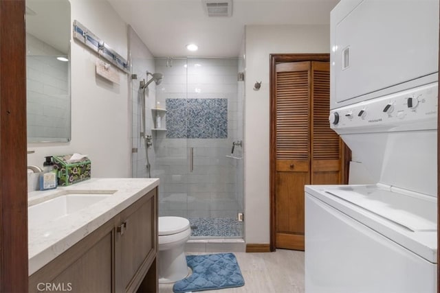 bathroom with wood-type flooring, toilet, stacked washer / drying machine, a shower with shower door, and vanity