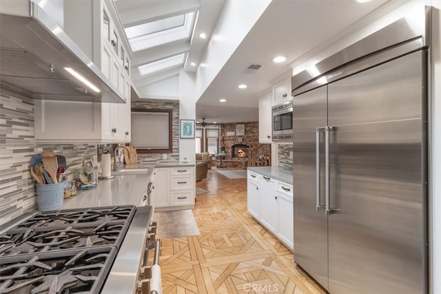 kitchen featuring decorative backsplash, wall chimney exhaust hood, built in appliances, sink, and white cabinets