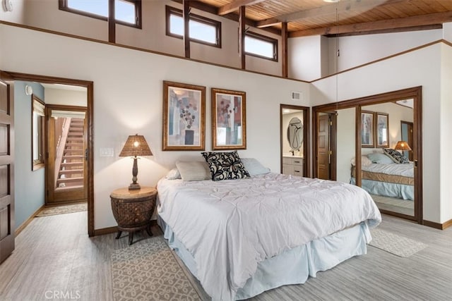 bedroom featuring connected bathroom, light hardwood / wood-style floors, beam ceiling, wooden ceiling, and high vaulted ceiling