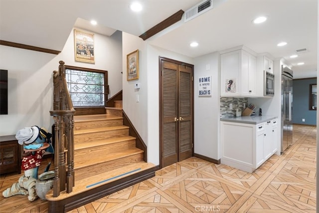 kitchen featuring backsplash, crown molding, white cabinets, appliances with stainless steel finishes, and light parquet flooring