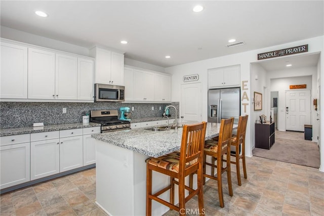 kitchen with white cabinets, sink, decorative backsplash, an island with sink, and appliances with stainless steel finishes