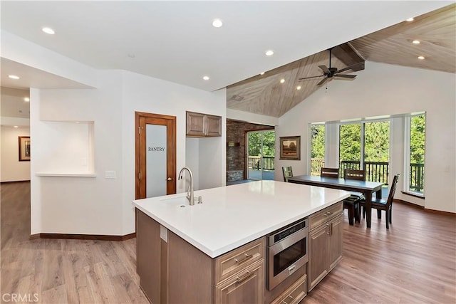 kitchen featuring ceiling fan, a kitchen island with sink, sink, light hardwood / wood-style flooring, and stainless steel microwave