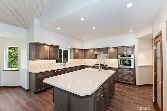 kitchen with a kitchen island with sink, dark hardwood / wood-style flooring, wall chimney range hood, and appliances with stainless steel finishes