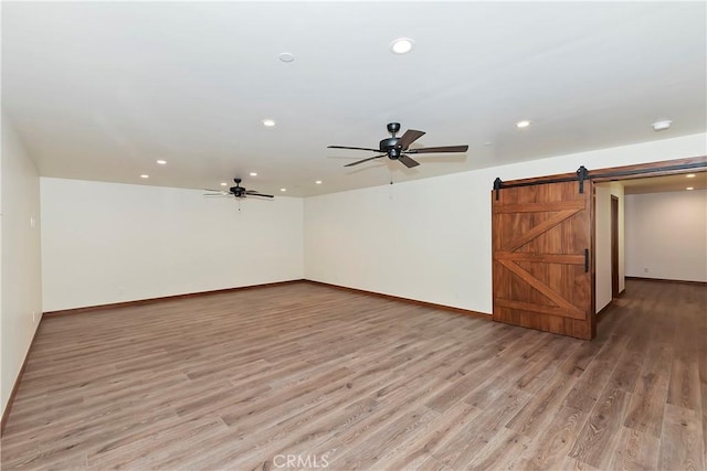 empty room featuring a barn door, ceiling fan, and light wood-type flooring