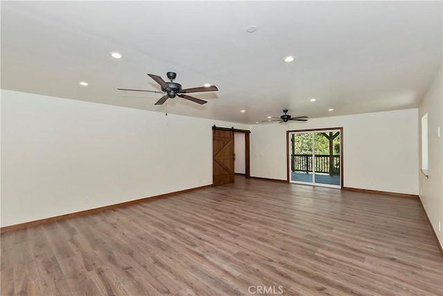 spare room with a barn door, light hardwood / wood-style floors, and ceiling fan