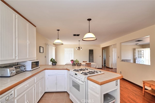 kitchen featuring white appliances, kitchen peninsula, white cabinetry, pendant lighting, and tile counters