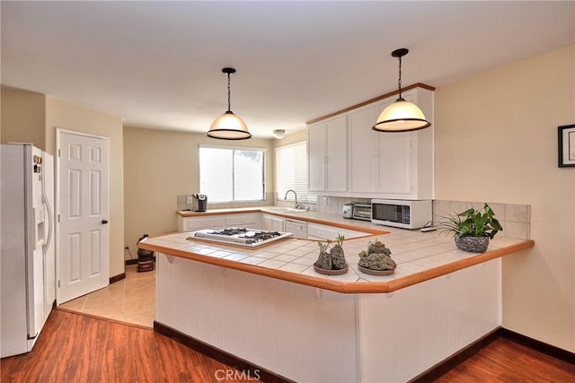 kitchen with white appliances, kitchen peninsula, tile counters, white cabinets, and hardwood / wood-style flooring