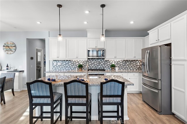 kitchen with white cabinetry, hanging light fixtures, stainless steel appliances, and light wood-type flooring