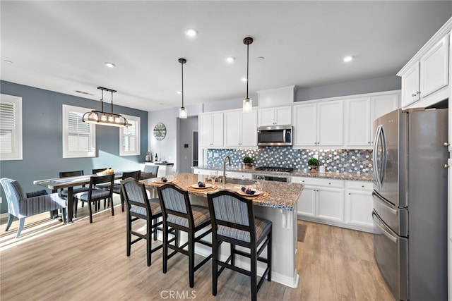 kitchen with white cabinets, appliances with stainless steel finishes, hanging light fixtures, and a kitchen island with sink