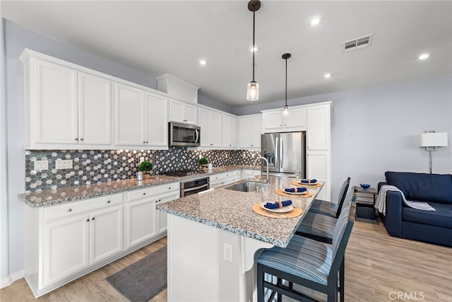 kitchen featuring sink, stainless steel appliances, a center island with sink, white cabinets, and light wood-type flooring