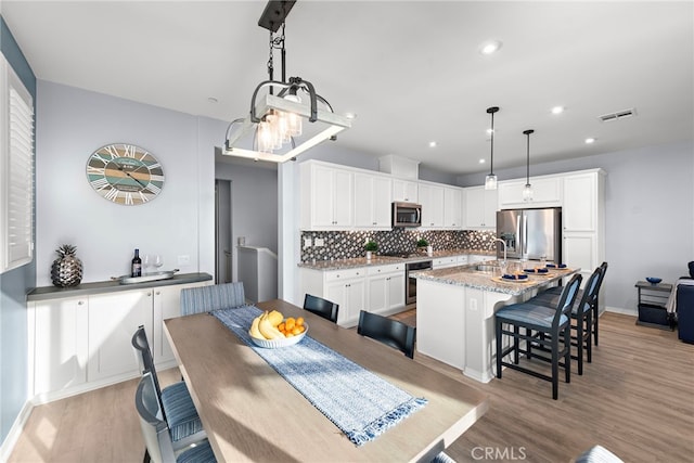 kitchen featuring a breakfast bar, white cabinets, appliances with stainless steel finishes, decorative light fixtures, and light hardwood / wood-style floors