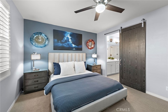 bedroom with a barn door, ceiling fan, ensuite bath, and light colored carpet