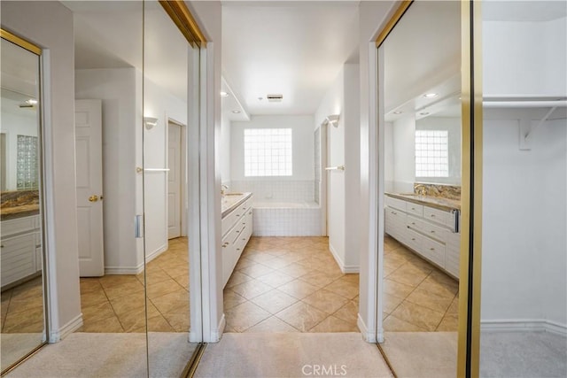 bathroom featuring tile patterned flooring, a relaxing tiled tub, plenty of natural light, and vanity