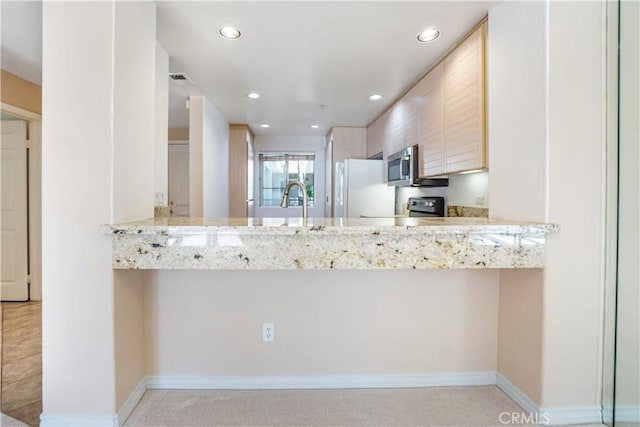 kitchen with kitchen peninsula, light brown cabinets, white refrigerator, and light stone counters