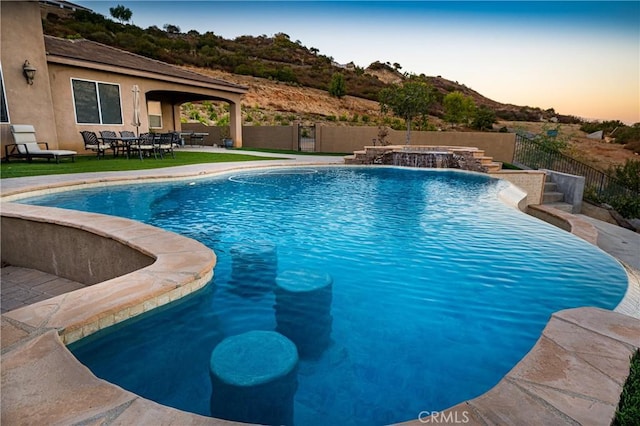 pool at dusk with pool water feature, a patio area, and a jacuzzi