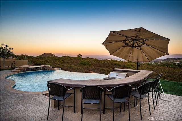 pool at dusk with pool water feature, an outdoor bar, an in ground hot tub, and a patio