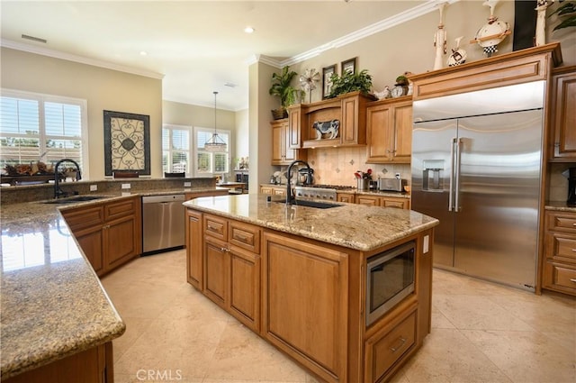 kitchen featuring pendant lighting, built in appliances, plenty of natural light, and a kitchen island with sink