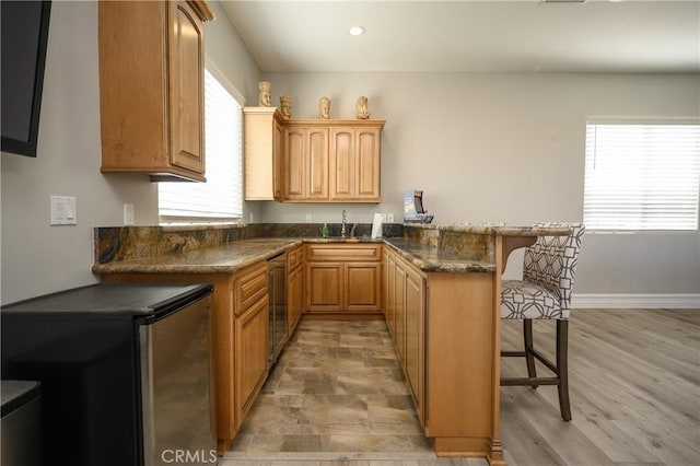 kitchen featuring kitchen peninsula, a breakfast bar, sink, dark stone countertops, and light hardwood / wood-style floors