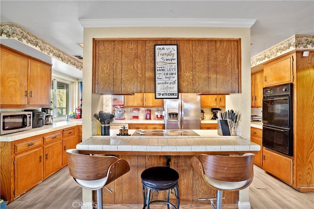 kitchen featuring appliances with stainless steel finishes, ornamental molding, light wood-type flooring, and a breakfast bar area