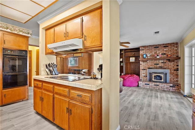 kitchen featuring tile countertops, black appliances, crown molding, and light wood-type flooring