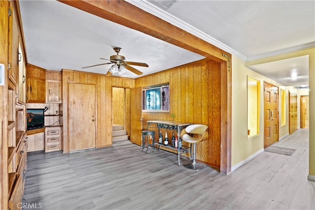 interior space with ceiling fan, a textured ceiling, ornamental molding, light hardwood / wood-style floors, and wooden walls