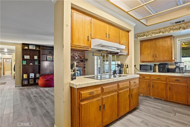 kitchen with ornamental molding, black electric stovetop, light hardwood / wood-style flooring, and a brick fireplace