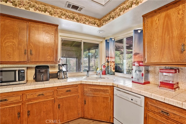 kitchen featuring tile counters, dishwasher, sink, and light wood-type flooring